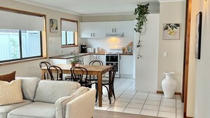 A modern living room with a sofa, a dining table with chairs, and a kitchen area in the background.