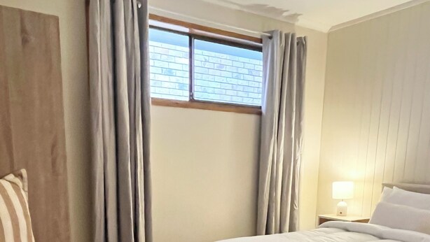 A hotel room with a bed, a bedside table with a lamp, and a window with curtains. - Casa Al Mare-your cosy beach house family and pet friendly central to everything (Burleigh Waters)