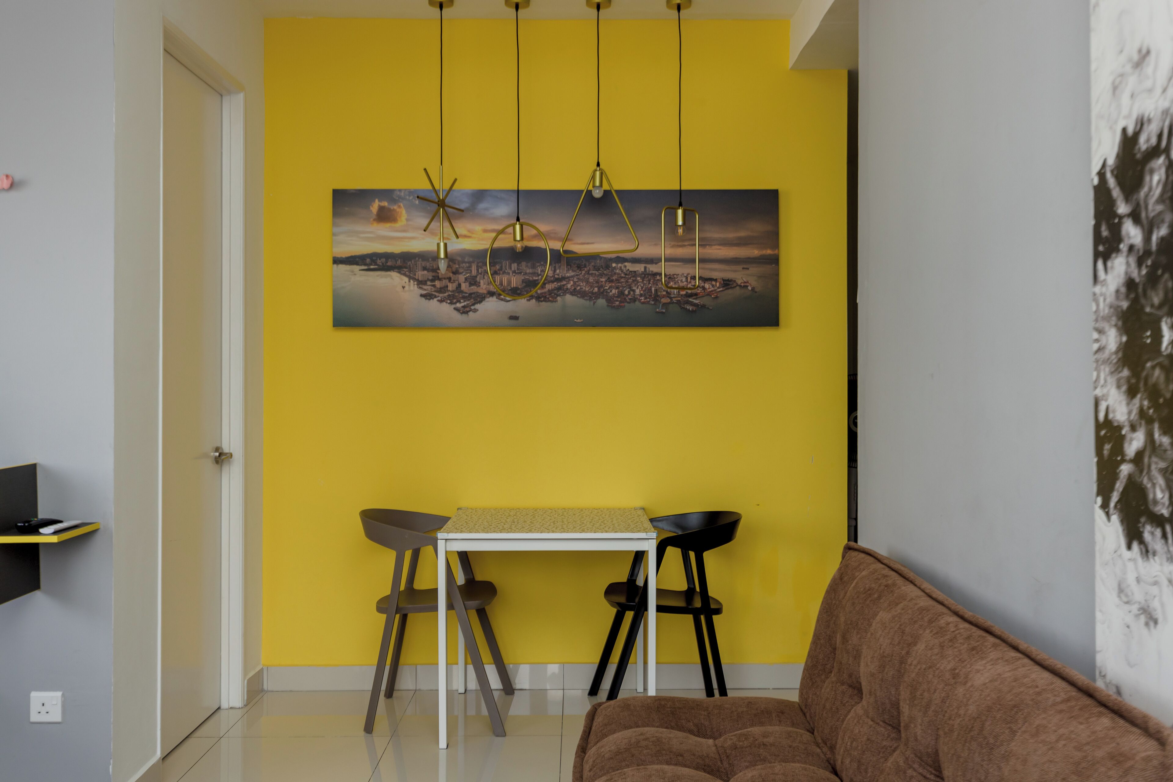 Uma sala de jantar com parede amarela, uma mesa, quatro cadeiras e um sofá marrom.