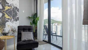A modern living room with a grey sofa, a small wooden table, and a large window with a view of a balcony and buildings. - ArteS Suite Penang (George Town)
