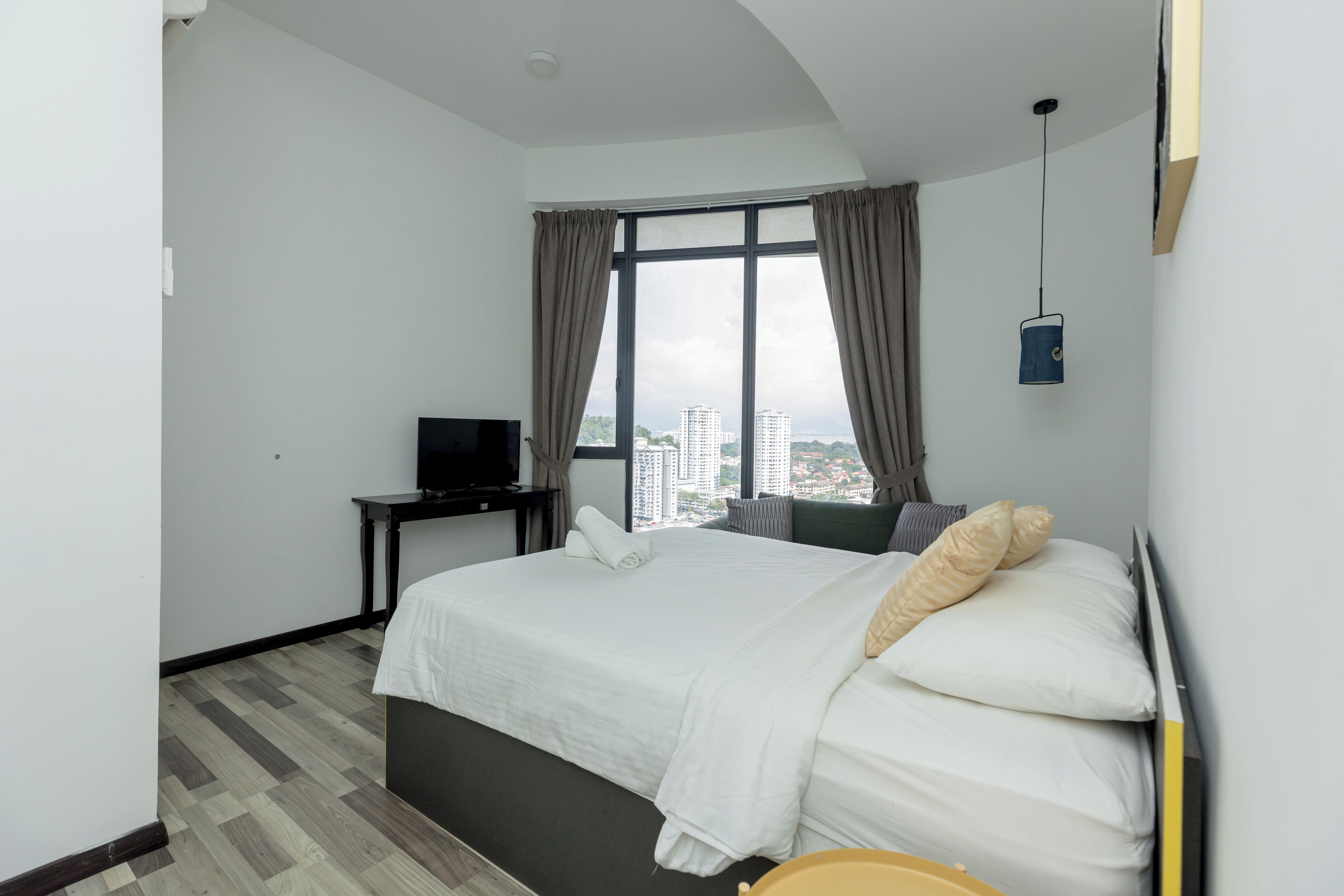 Una habitació d'hotel amb un llit gran, un televisor sobre una taula petita i vista a la ciutat a través de grans finestres.