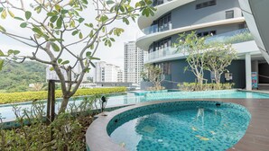 A modern building with a curved swimming pool, surrounded by greenery and a view of a cityscape. - ArteS Suite Penang (George Town)