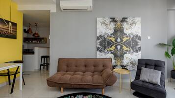 Un soggiorno con un divano marrone, una poltrona nera, un grande quadro astratto e un angolo cucina sullo sfondo.