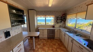 A kitchen with a view of the ocean, a sink, a stove, and a countertop.