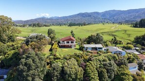 A rural property with a large house surrounded by lush greenery and mountains in the background.