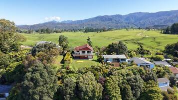 A rural property with a large house surrounded by lush greenery and mountains in the background.