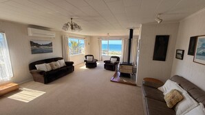 A spacious living room with a sofa, armchairs, and a coffee table. There are large windows with a view of the sea.