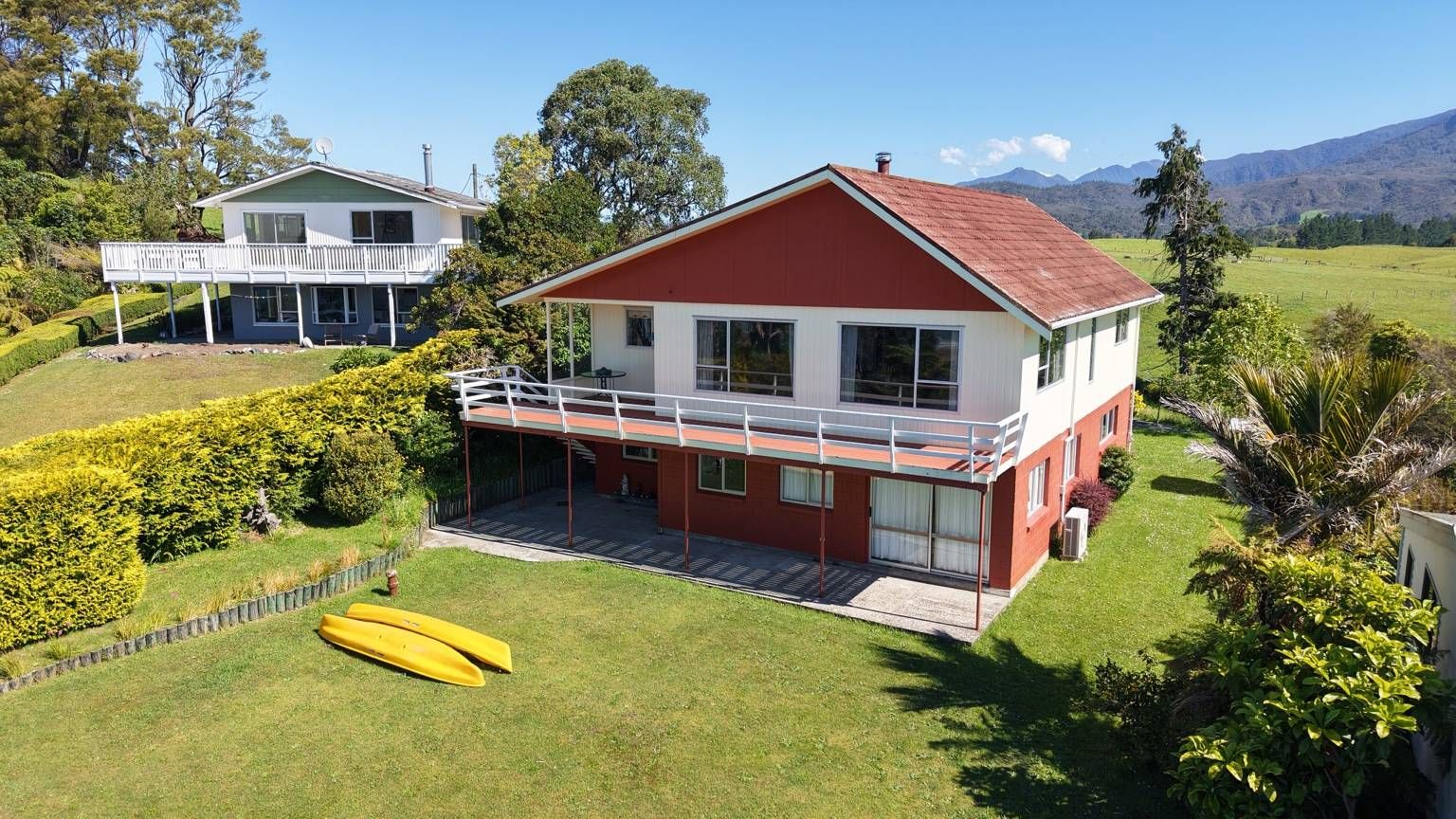 A two-story house with a balcony, surrounded by well-maintained gardens and a mountainous backdrop.