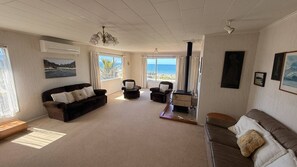 A spacious living room with a sofa, armchairs, and a coffee table. There are large windows with a view of the sea. - Seaview Escape in Patons Rock (Patons Rock)