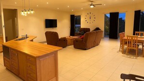 Uma sala de estar moderna com uma mesa de jantar de madeira, dois sofás, uma televisão e um ventilador de teto.