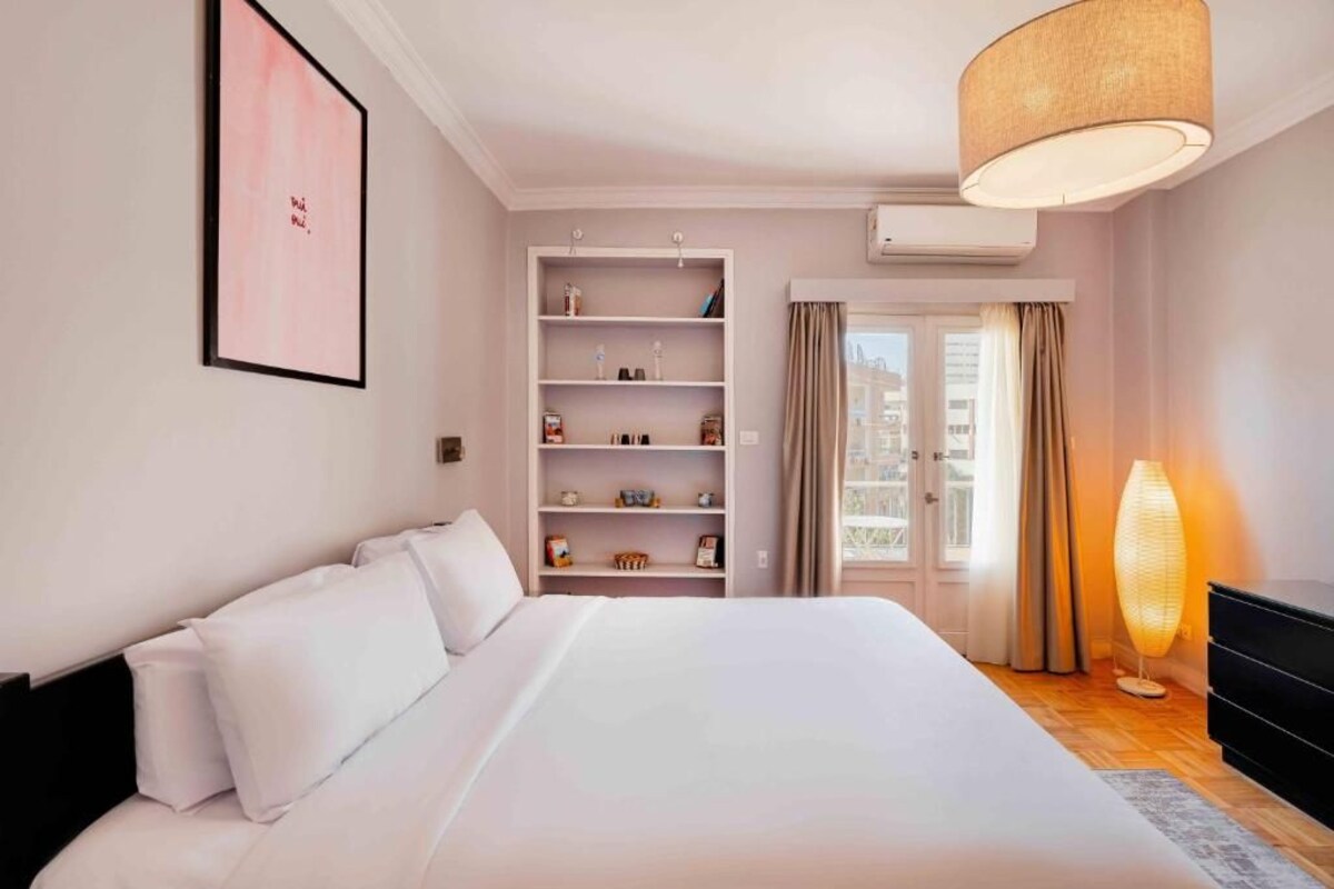 Un dormitorio con una cama grande, una estantería empotrada, una lámpara de noche y vistas a través de una puerta.
