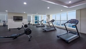 Een moderne sportschool met loopbanden, hometrainers en roeïngmachines, met grote ramen en uitzicht over de stad.