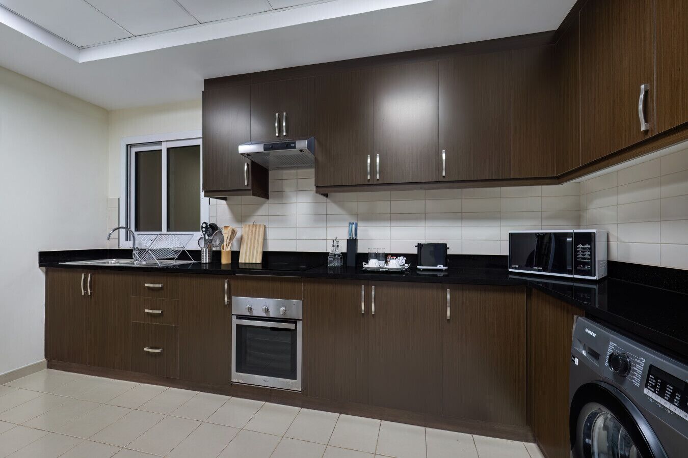 A modern kitchen with dark wooden cabinets, a stainless steel oven, a microwave, and a washing machine.