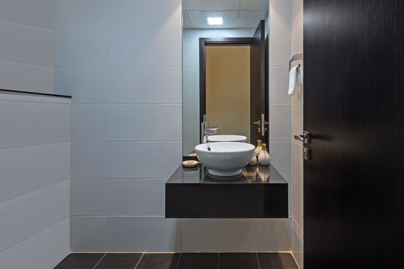 Une salle de bain moderne avec un plan de toilette noir, deux vasques blanches et un miroir au-dessus.