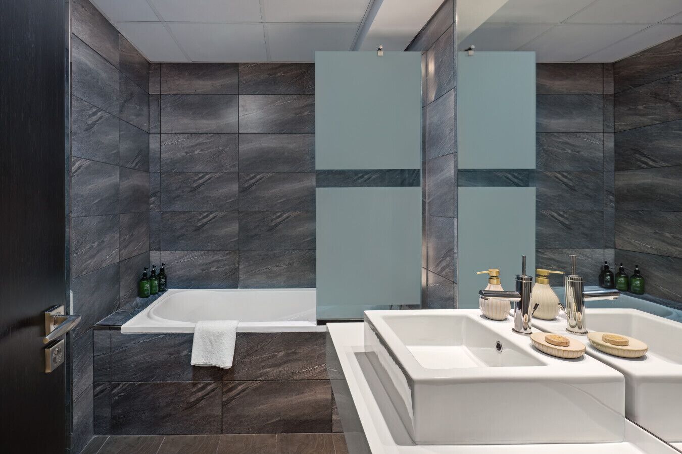 A modern bathroom with a bathtub, a large mirror, and a vanity with a sink and multiple bottles.