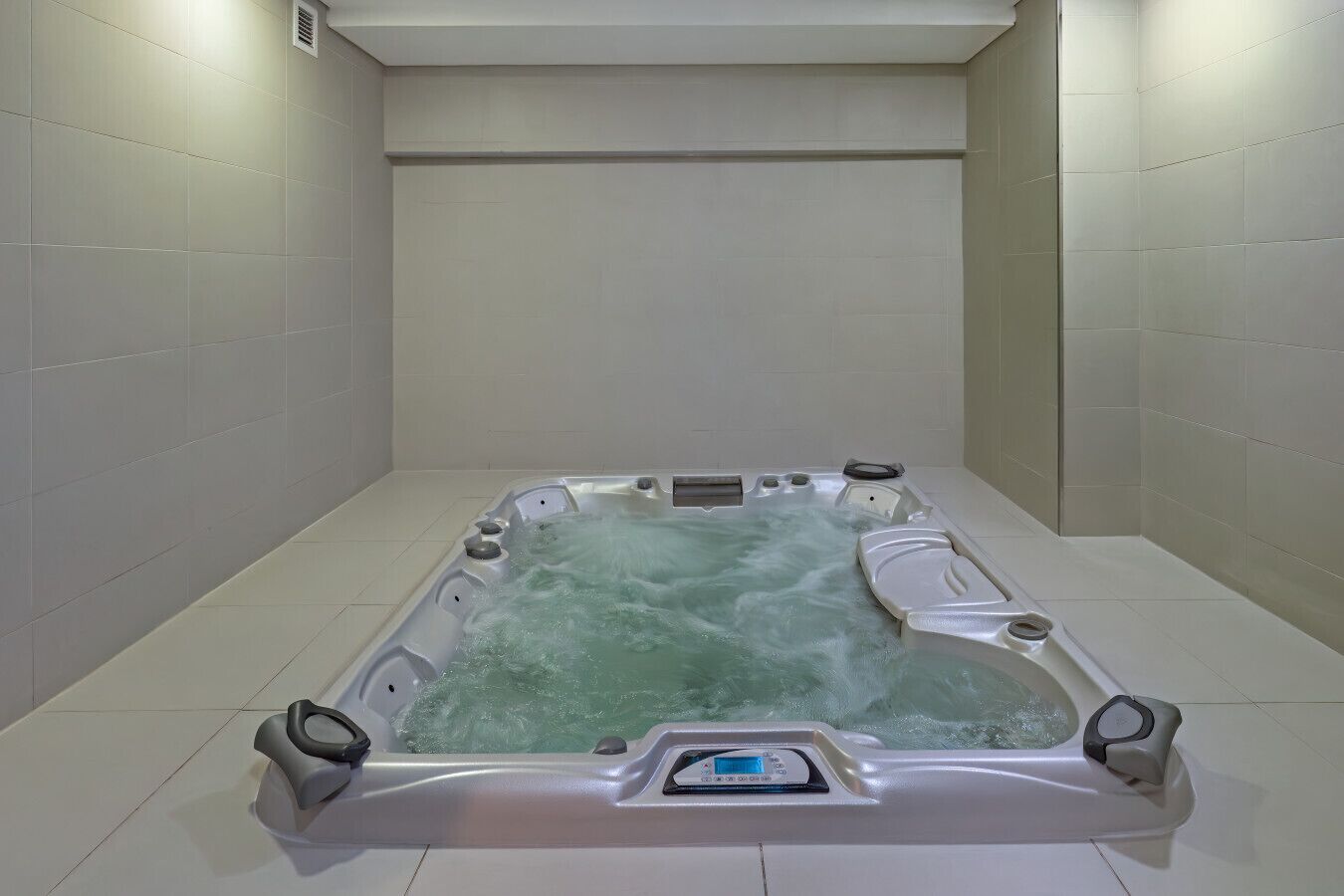 Ein rechteckiges Whirlbad mit einer Bedienkonsole in der Mitte, umgeben von weißen Fliesenwänden und -böden.