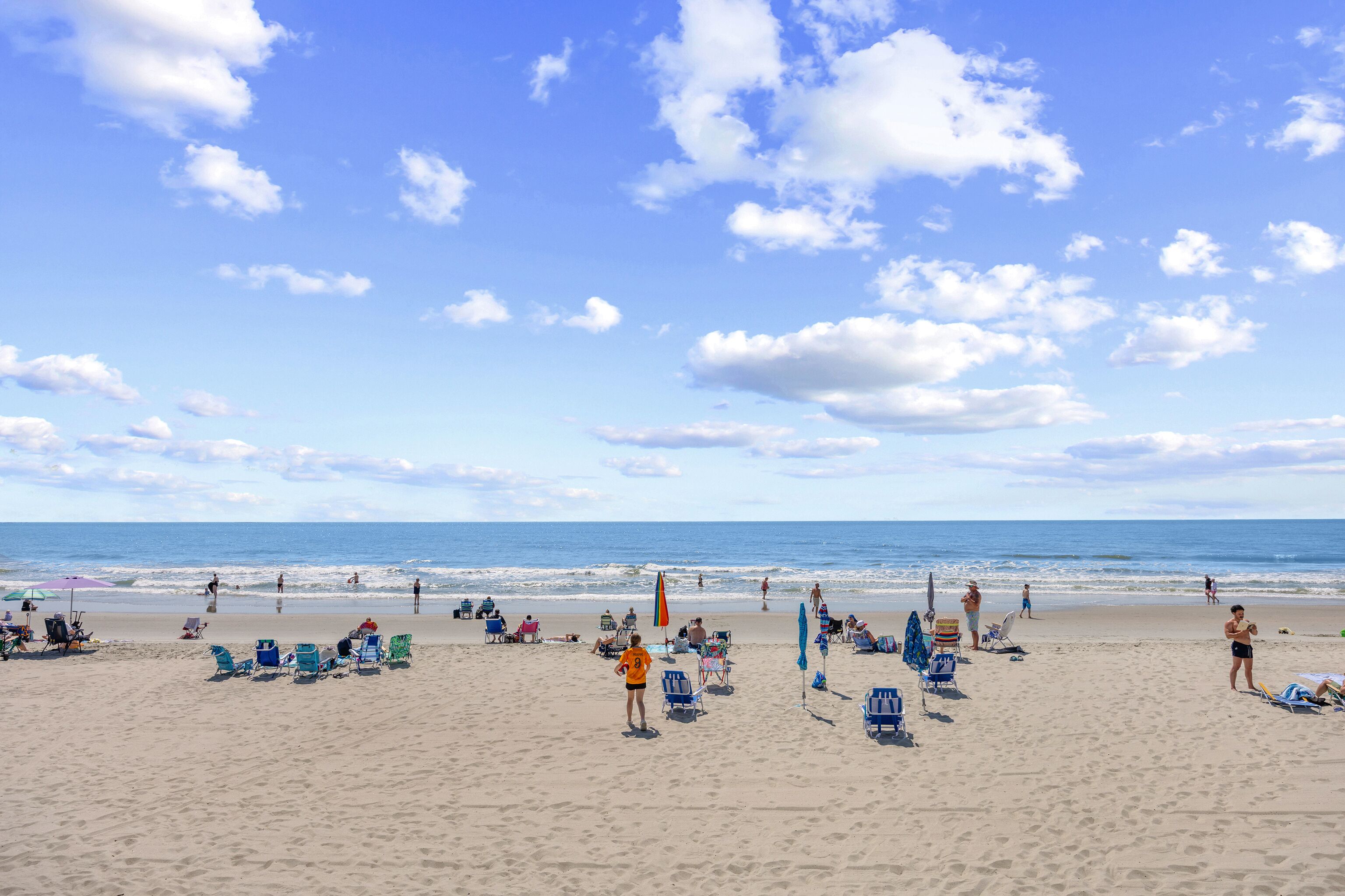 Ein Strand mit Menschen, Stühlen und Sonnenschirmen.