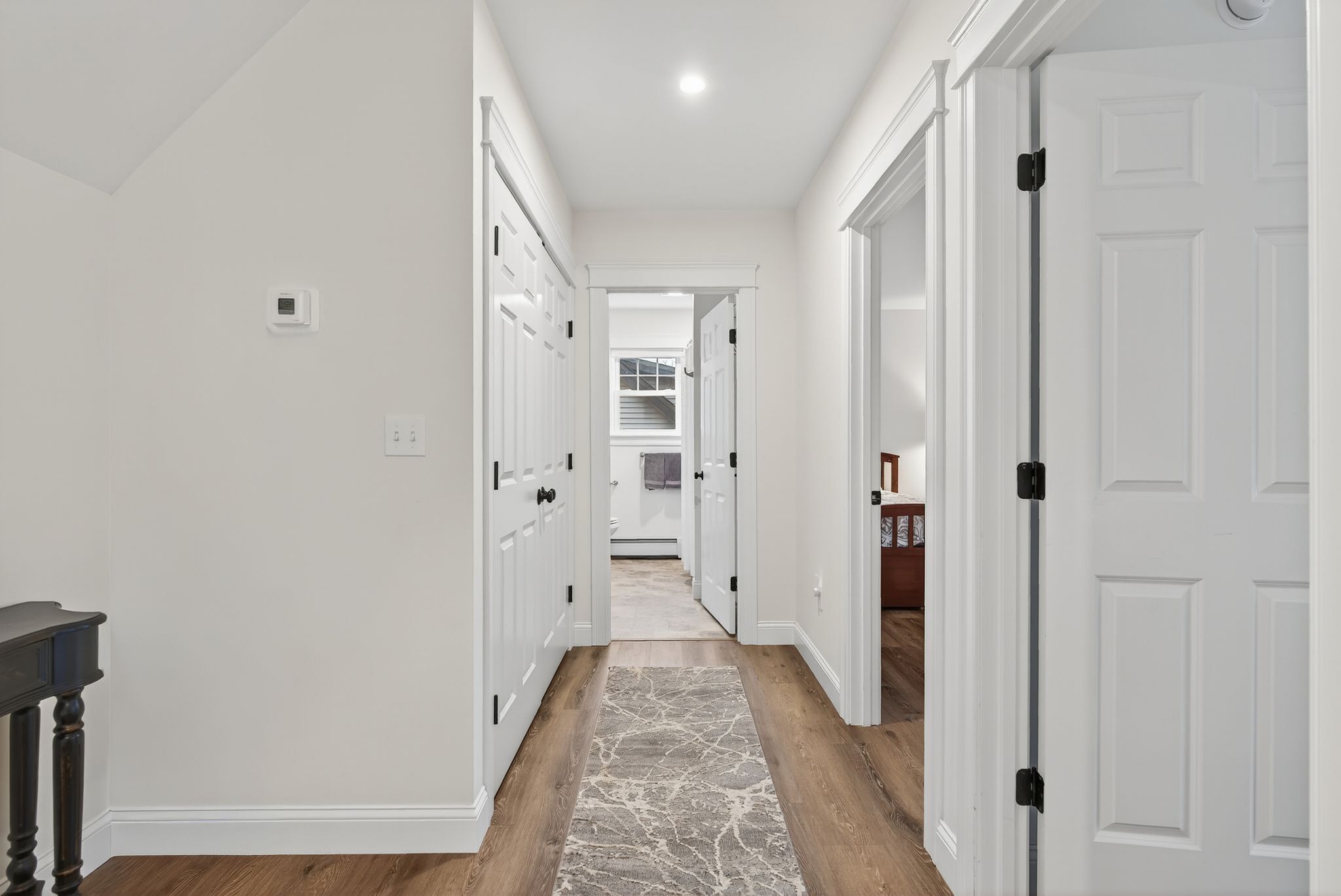 A hallway with white doors, a marble-patterned rug, and a wooden floor.