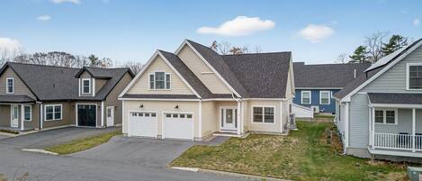 A row of single-family homes with attached garages, a well-maintained lawn, and a clear sky.