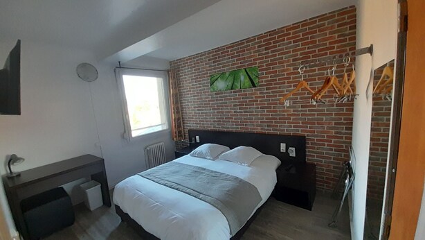 Une chambre moderne avec un mur en briques, un lit, une fenêtre, un bureau et un radiateur.