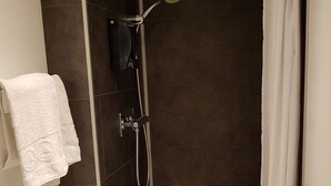 Une salle de bain avec des toilettes, une douche dotée d’une porte en verre et une serviette blanche accrochée au mur.