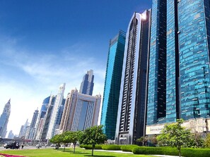 A cityscape with modern high-rise buildings, a clear sky, and a well-maintained park area with trees and a pathway. - Elevate Your Escape: Luxurious Vacation Homes (Dubai)