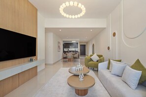 A modern living room with a flat-screen TV, a round coffee table, a sofa with cushions, and a dining area in the background. - Elevate Your Escape: Luxurious Vacation Homes (Dubai)