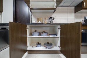 A kitchen with open wooden cabinets containing pots and pans. - Elevate Your Escape: Luxurious Vacation Homes (Dubai)