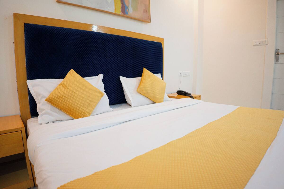 A hotel room with a bed, a nightstand, a telephone, and a wall socket.