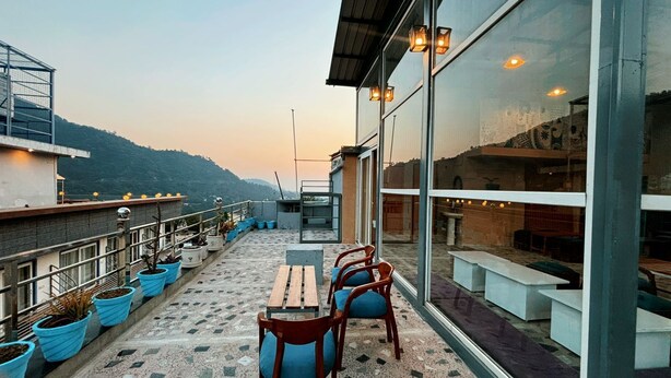 A rooftop terrace with a table and chairs, potted plants, and a view of the surrounding landscape.