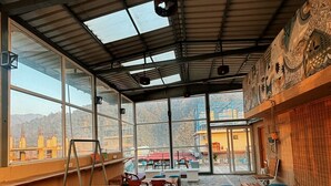 An indoor seating area with tables and benches, large windows, and a view of the city.