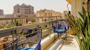 Un balcon avec des chaises bleues, un pot de fleurs et une vue sur les immeubles de la ville.