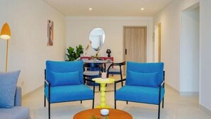 Un salon moderne avec deux fauteuils bleus, une table basse ronde et un coin repas comprenant une table et des chaises.
