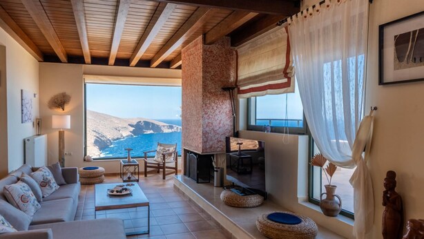 Un salon spacieux doté d’une grande fenêtre offrant une vue panoramique sur la mer et les montagnes.