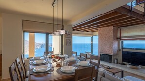 Un espace repas avec vue sur la mer, des poutres en bois et une cheminée.