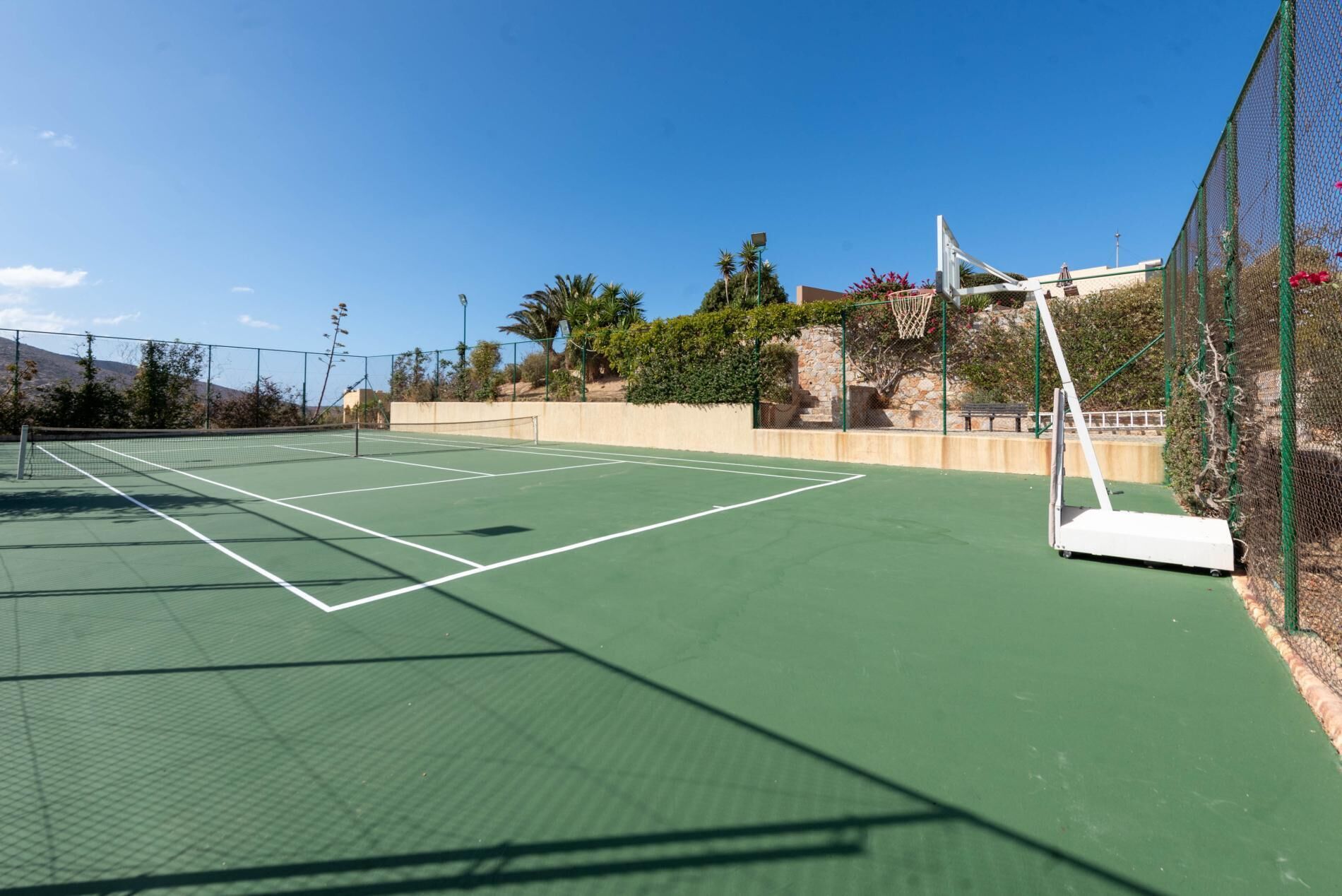 A tennis court with a net, surrounded by a fence and greenery.
