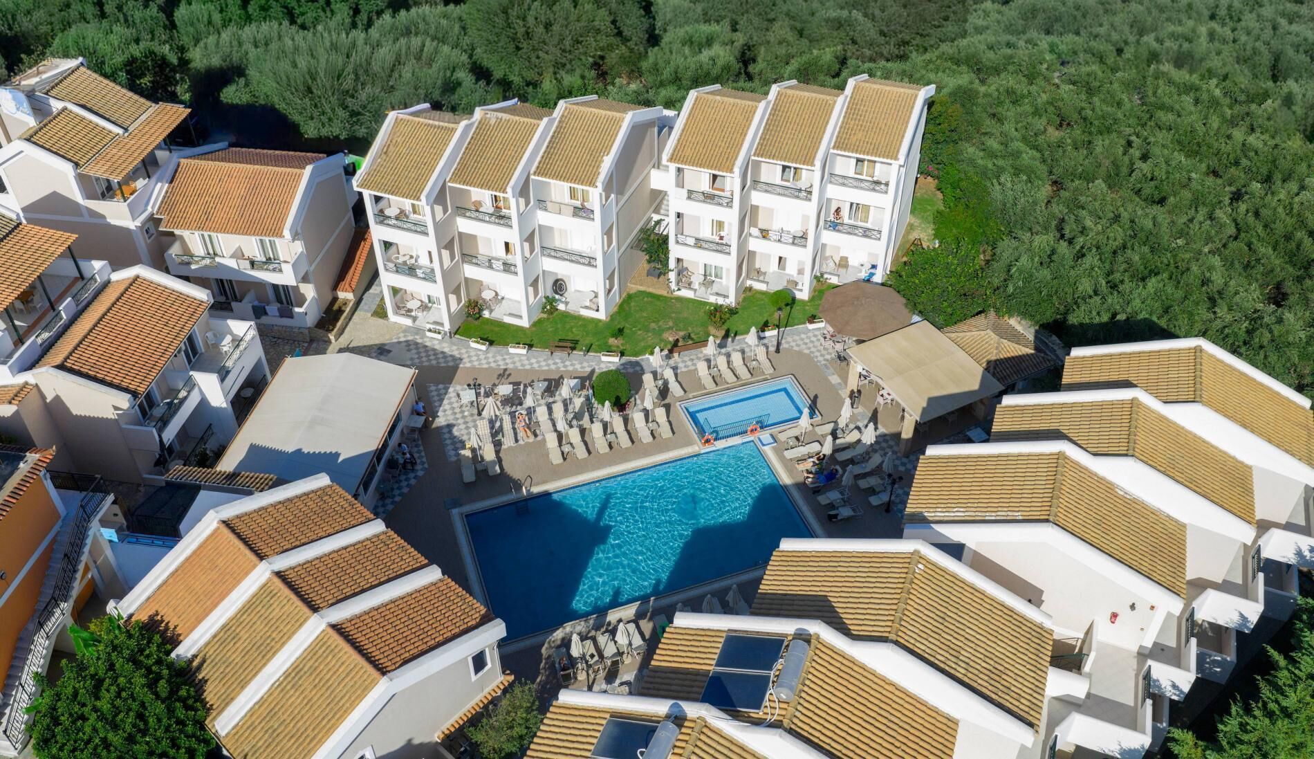 An aerial view of a resort with multiple buildings, a central swimming pool, and surrounding greenery.