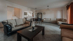 A spacious living room with a dark wooden coffee table, two sofas, and a dining area with a chandelier. - Dream House in Tragaki (Zakynthos)