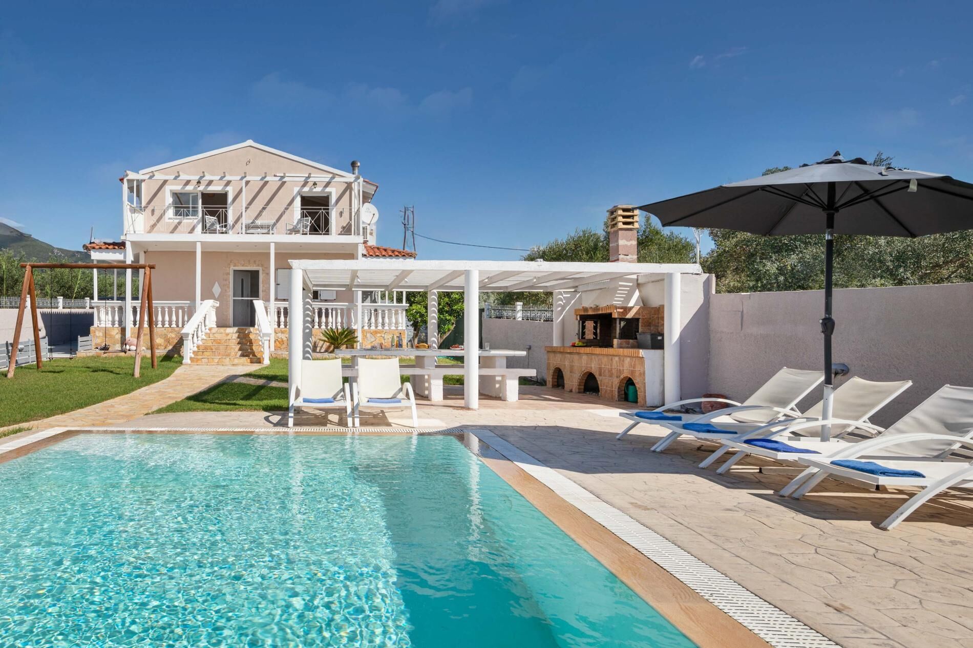 A pool area with a clear pool, lounge chairs, and a barbecue setup.
