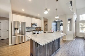 Una cocina moderna con electrodomésticos de acero inoxidable, una isla de granito e iluminación colgante.