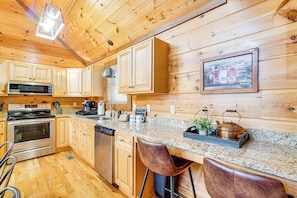 A kitchen with wooden cabinets, a granite countertop, a stainless steel oven, a microwave, a coffee maker, and a kettle. - 2 Mi to Downtown Gatlinburg: Cabin w/ Game Room! (Gatlinburg)