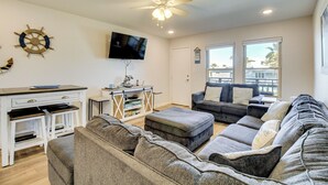 A living room with a grey sofa, a white coffee table, a TV mounted on the wall, and a ceiling fan. - Steps to Sand: Breezy Port Aransas Condo! (Port Aransas)