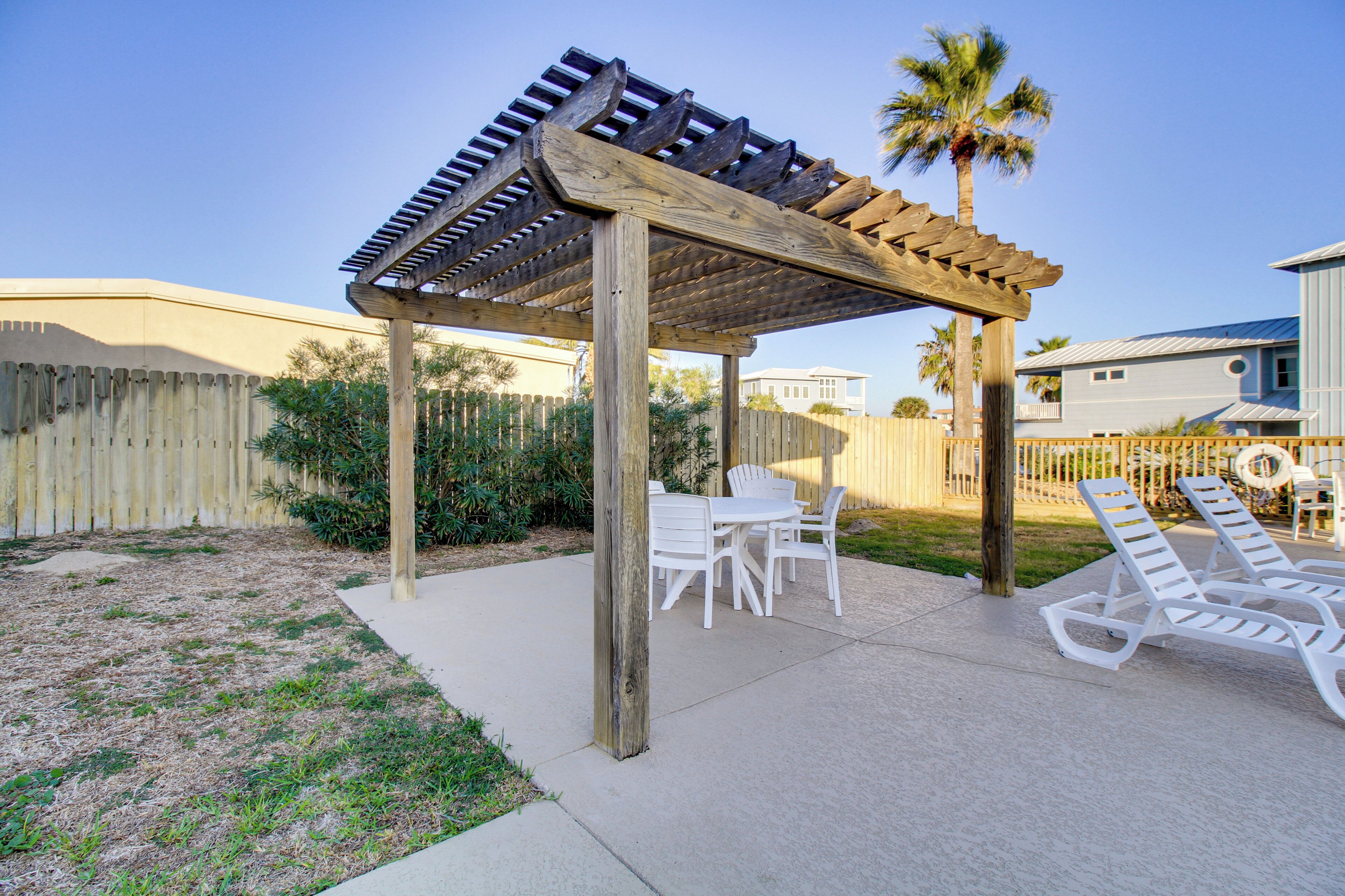 A covered patio with a table and chairs, a poolside area with lounge chairs, and a wooden pergola.