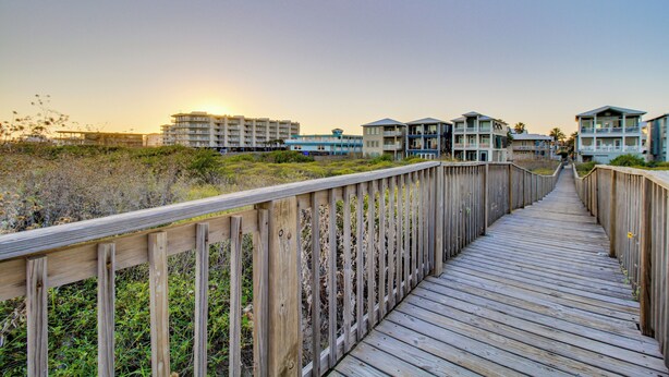 A wooden boardwalk leading to beachfront buildings with balconies, surrounded by natural vegetation. - Steps to Sand: Breezy Port Aransas Condo! (Port Aransas)