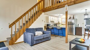 A modern living room with a blue sofa, wooden staircase, and a kitchen area with bar stools. - Ski, Swim & Hike! Family Home in Tobyhanna (Tobyhanna)
