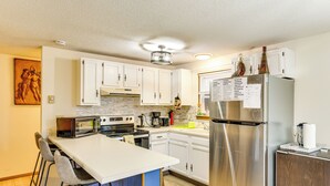 A modern kitchen with white cabinets, a stainless steel refrigerator, a bar area with stools, and a microwave. - Ski, Swim & Hike! Family Home in Tobyhanna (Tobyhanna)