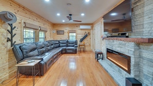 A log cabin interior with a leather sectional sofa, a fireplace, and a mounted TV. - Big South Fork National River and Recreation Area (Oneida)