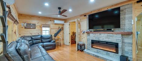 A cozy living room with a leather sectional sofa, a fireplace, and a flat-screen TV mounted on the wall.