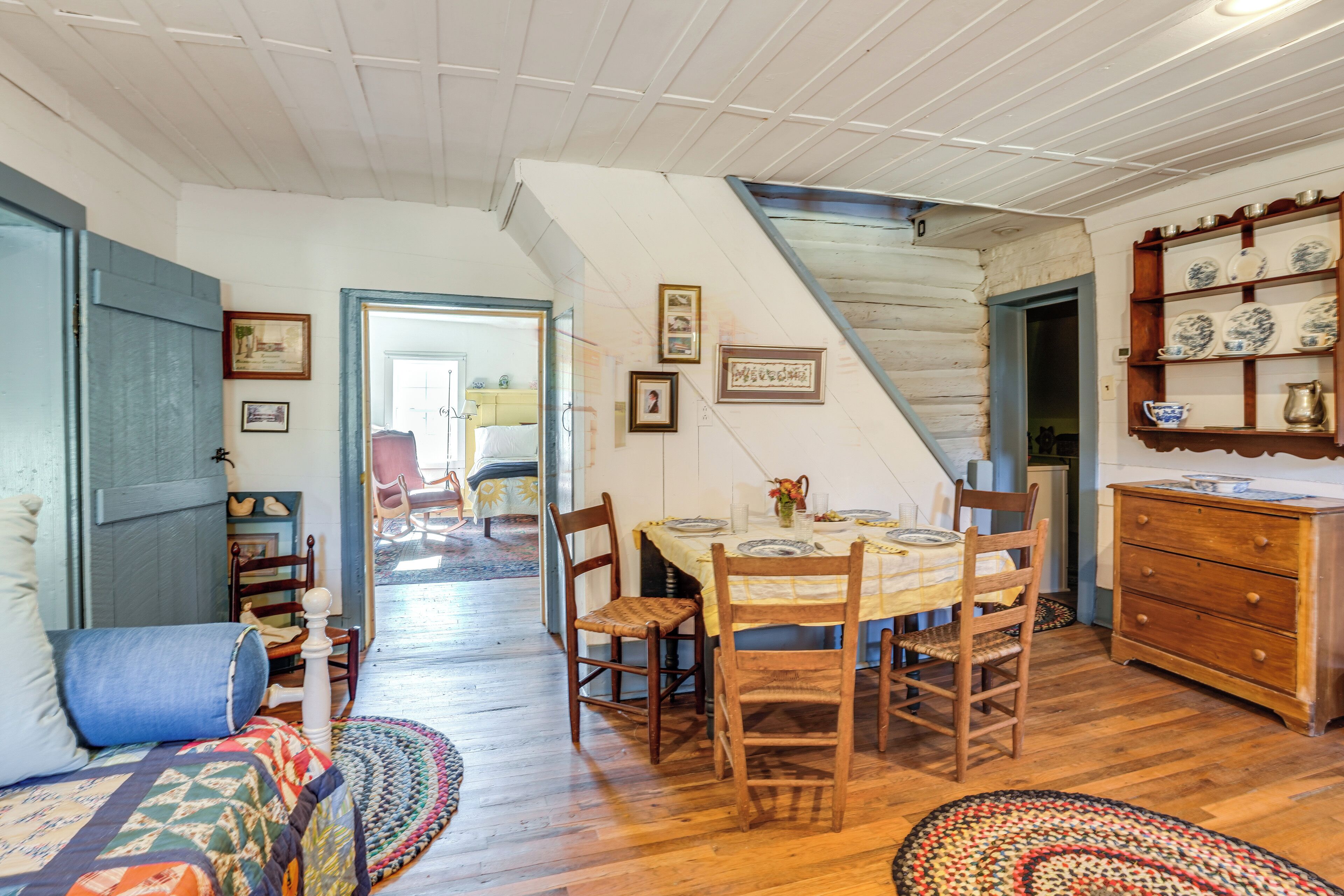 Un comedor acogedor con sillas de madera y una mesa dispuesta para dos personas, una escalera que conduce a otra habitación y un aparador de madera con platos decorativos.