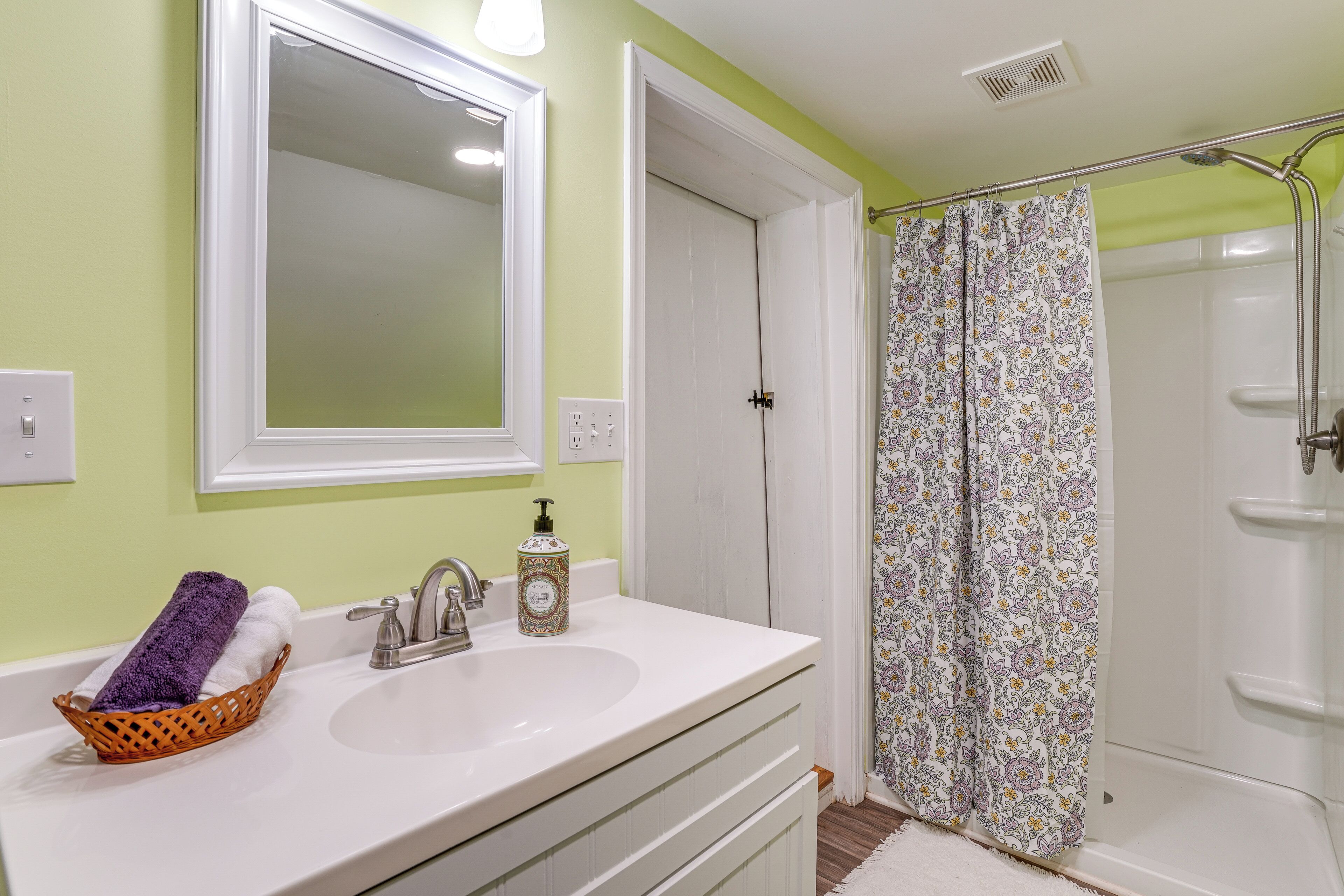 A bathroom with a white sink, a mirror, a shower curtain, and a basket with towels.